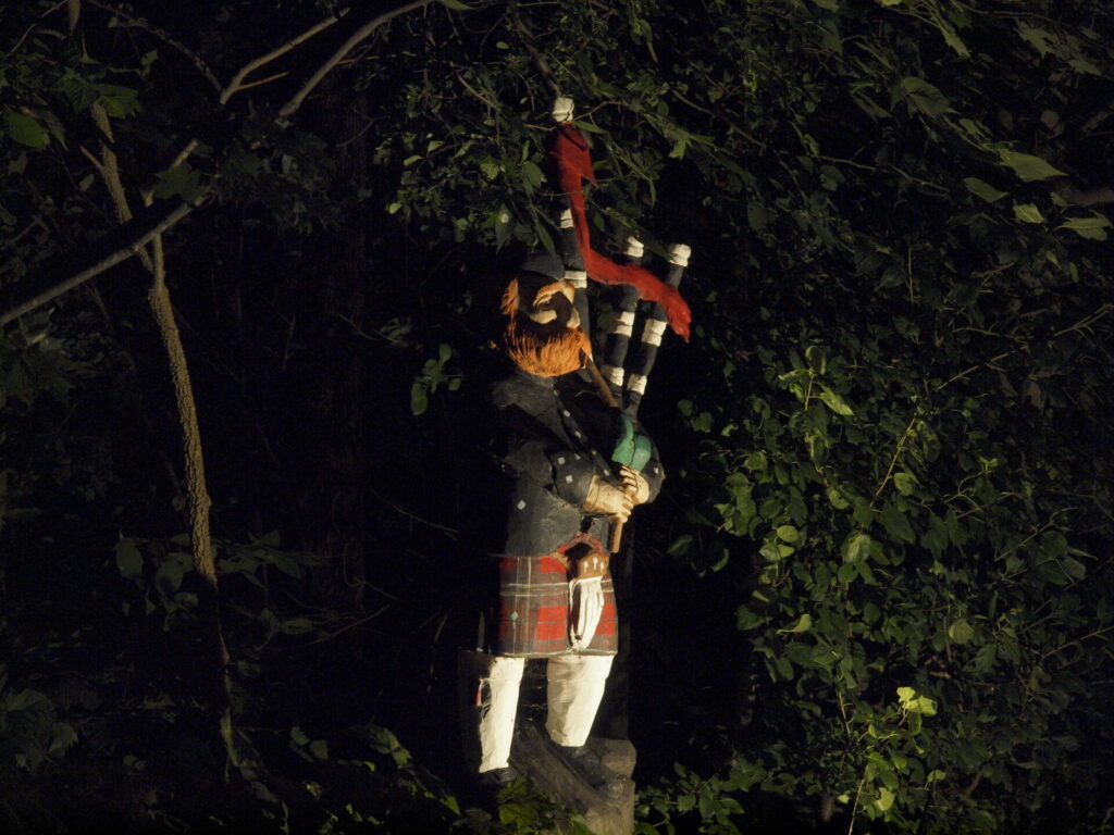 A statue of a bagpipe player lit up at night.
