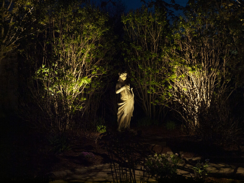 A statue in a garden lit up at night.