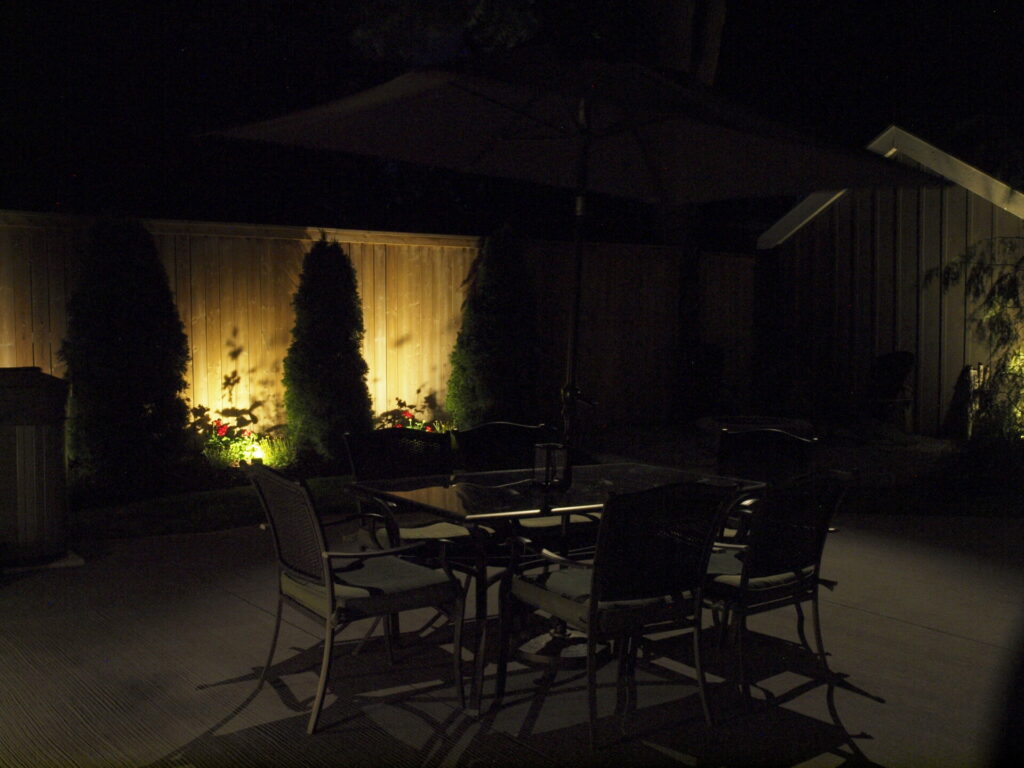 A table and chairs in a backyard at night with outdoor lights in the garden.