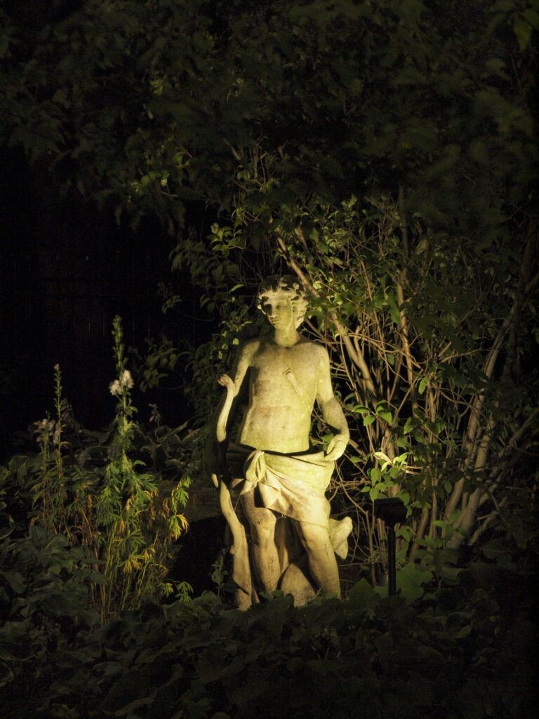 A statue in the middle of a wooded area at night lit up with outdoor lighting.