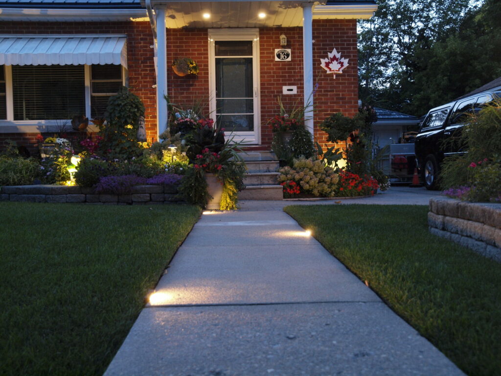 A red brick house is lit up by outdoor lighting in the garden.