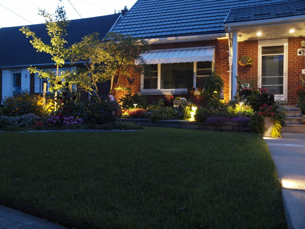 A red brick house is lit up by outdoor lighting in the garden.