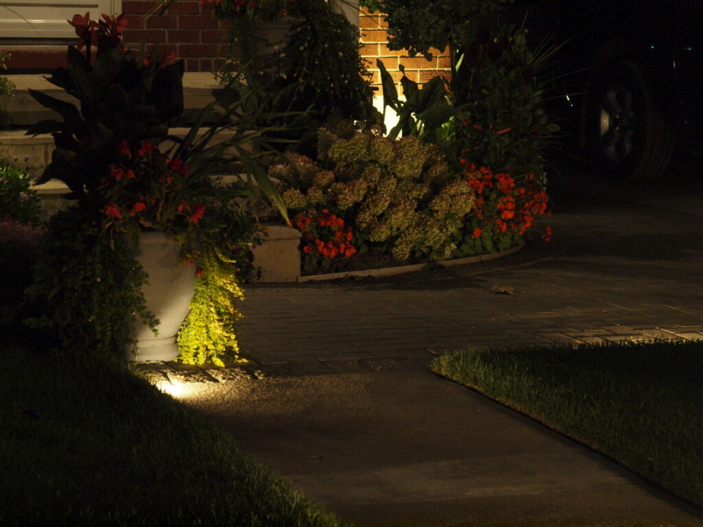 A walkway, big planter, and garden lit up at night.