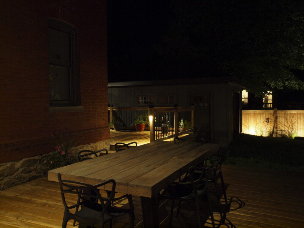 A wooden deck with a table and chairs with outdoor lighting at night.