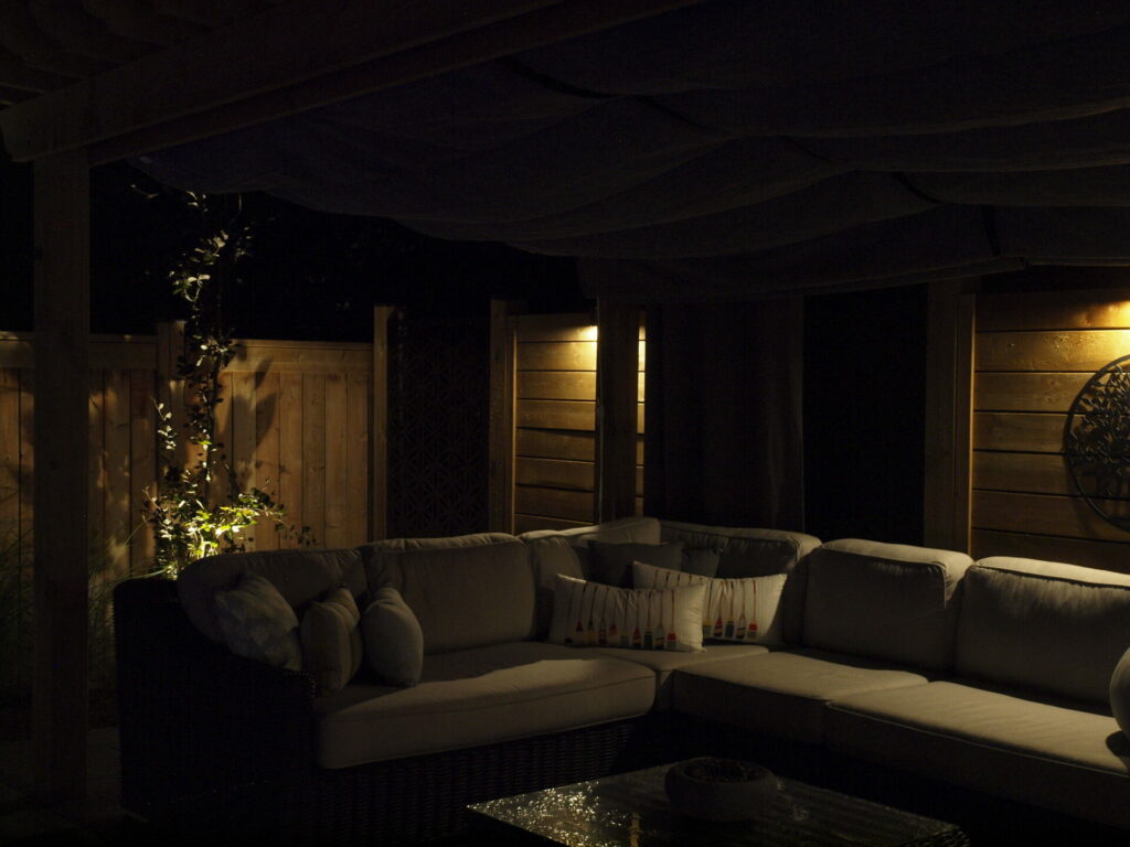 A big, gray sectional couch on a patio lit up at night with outdoor lighting.
