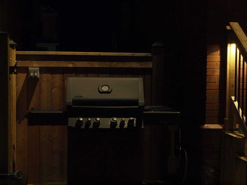 A bbq grill in front of a wooden fence lit up at night.