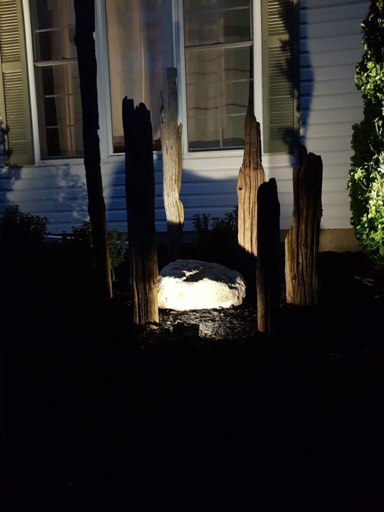 Wooden pieces and a big rock in front of a house lit up at night.