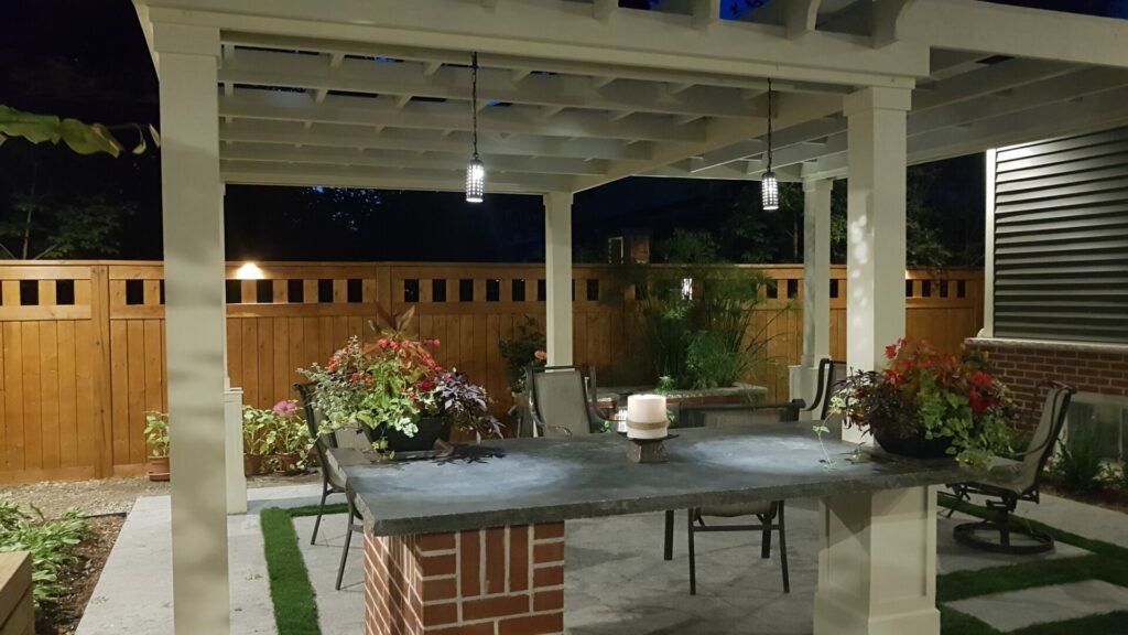 A backyard patio with a table and chairs with outdoor lighting at night.
