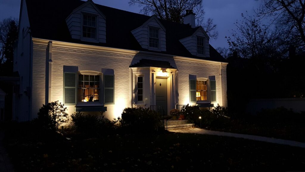 A white brick house is lit up at night with outdoor lighting.