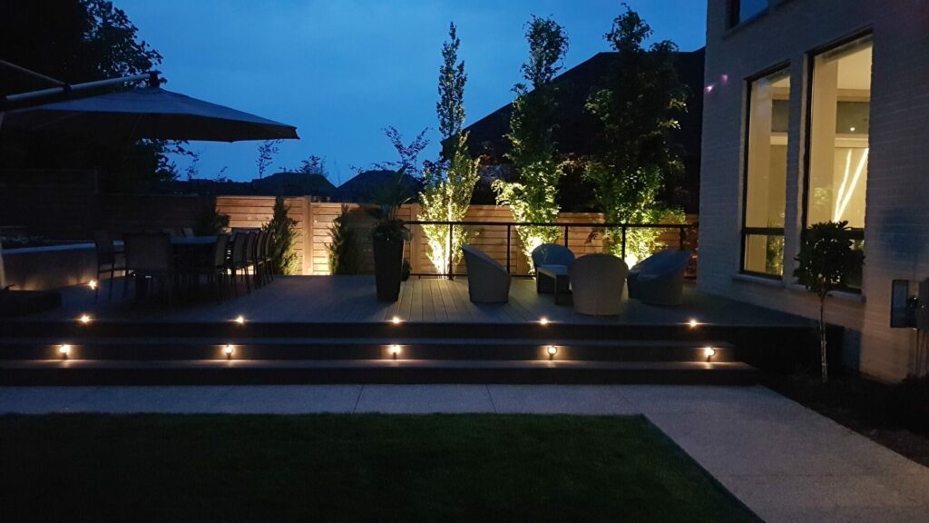 A backyard deck with two seating area with outdoor lighting at night.