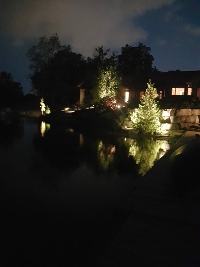 A house is lit up at night with a body of water.