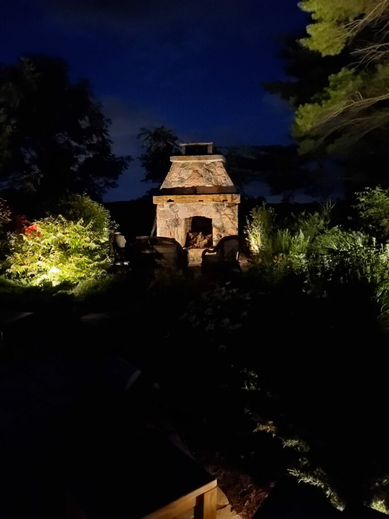 A stone fireplace lit up at night in a garden.