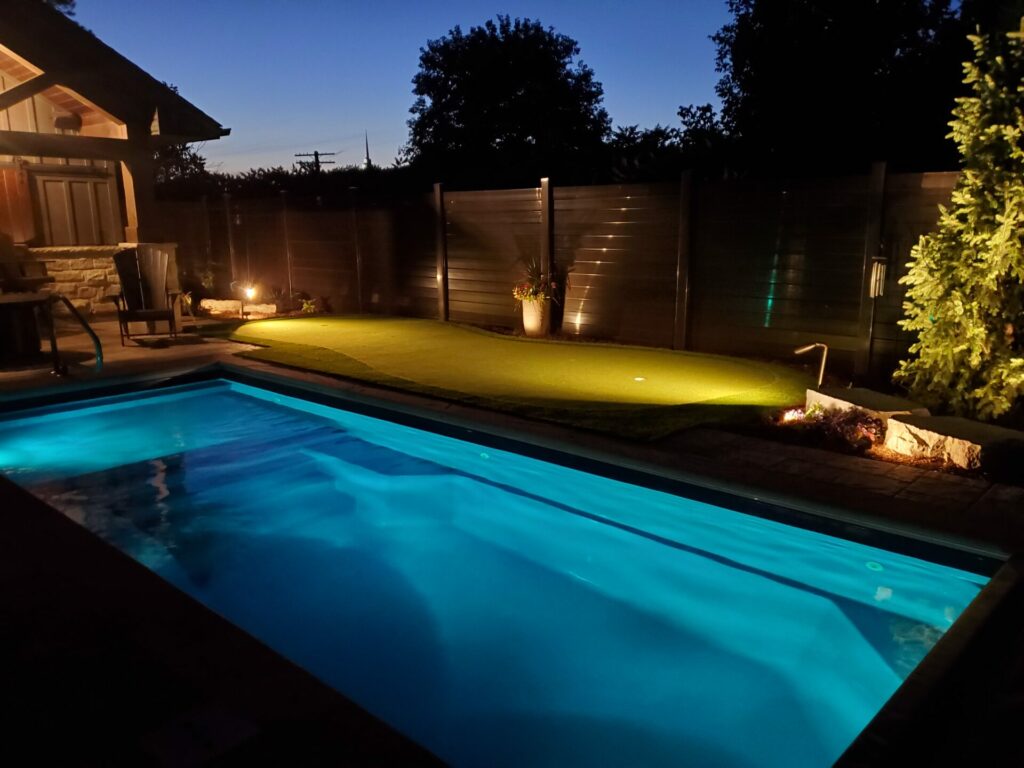 A backyard pool and mini putt hole lit up at night.