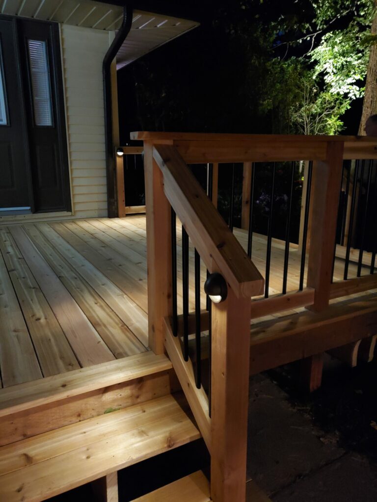 A wooden deck with a railing and lights at night.