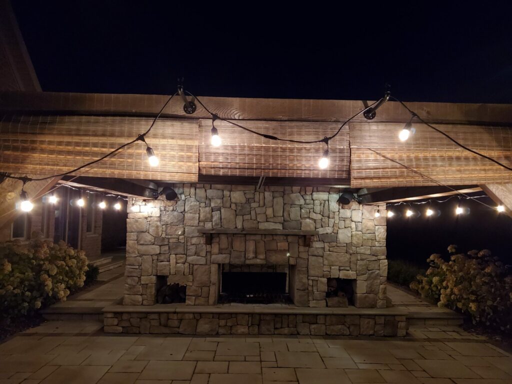 A patio with a fireplace and string lights at night.