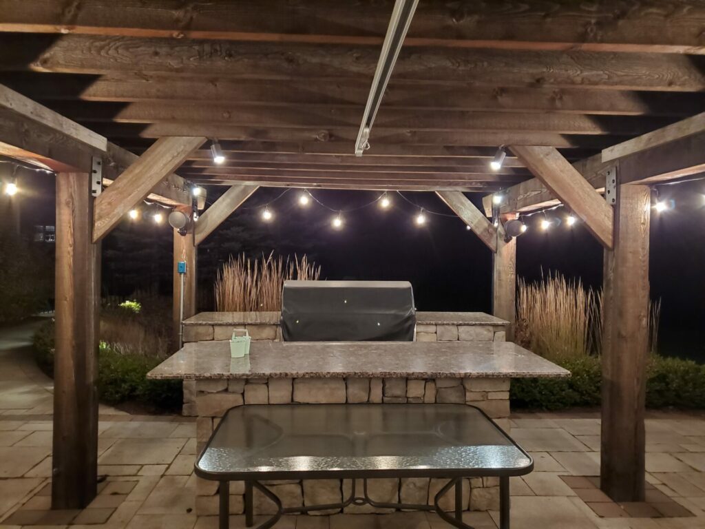 An outdoor kitchen with string lights and a grill lit up at night.