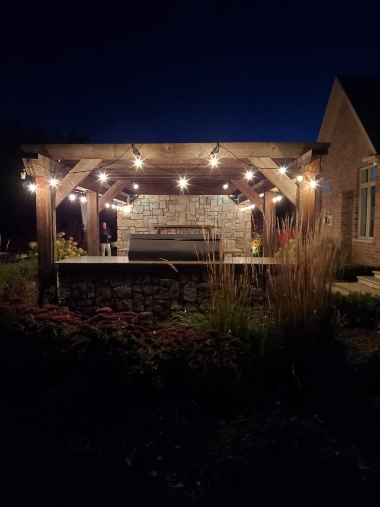 A pergola with string lights and a fire pit at night.