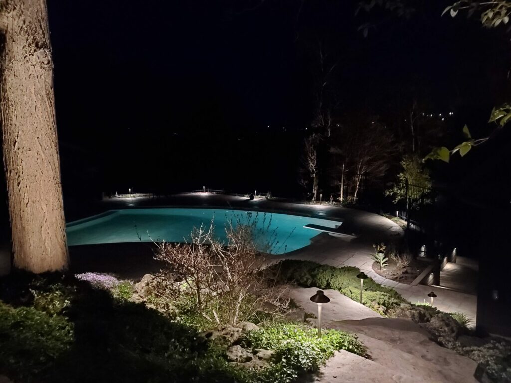 A swimming pool lit up at night in a wooded area.