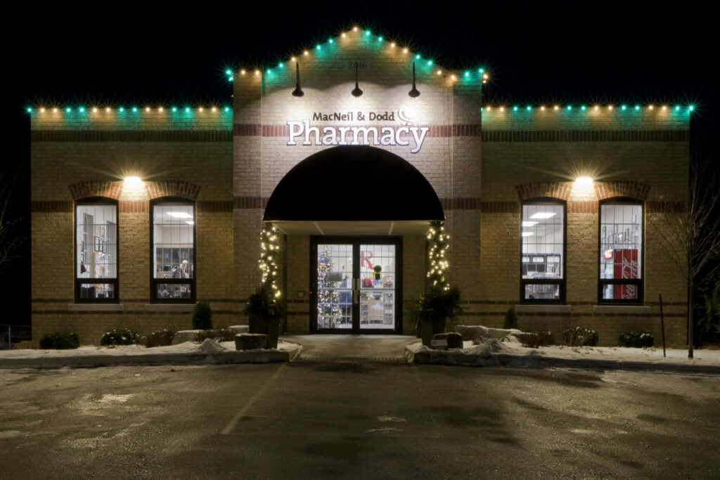 A pharmacy building lit up at night with Christmas lights and outdoor lights.