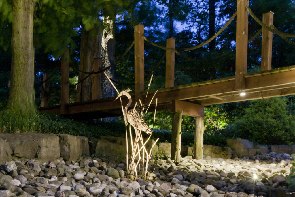 A wooden bridge in the middle of a garden at night.