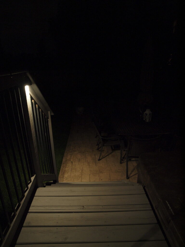 A wooden stairway with outdoor lighting in the dark.