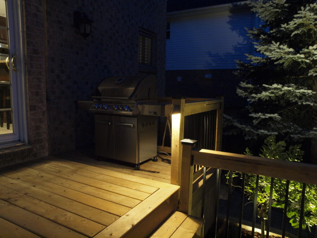 A wooden deck with a grill lit up at night.