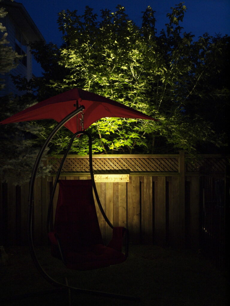 A red swing chair under an umbrella in a yard at night.