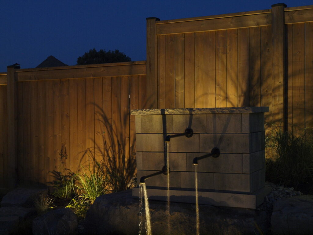 A wooden fence and three water spouts at night.