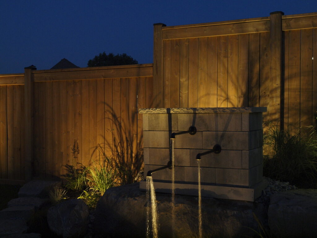 A wooden fence and three water spouts at night.