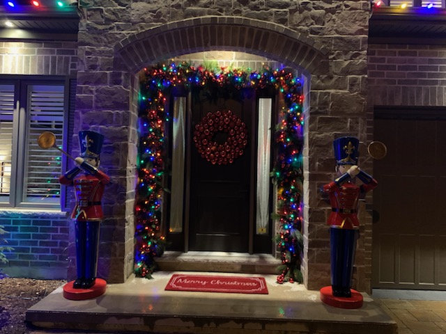 The front door of a home is decorated with Christmas lights and flanked by two big nutcracker statues.