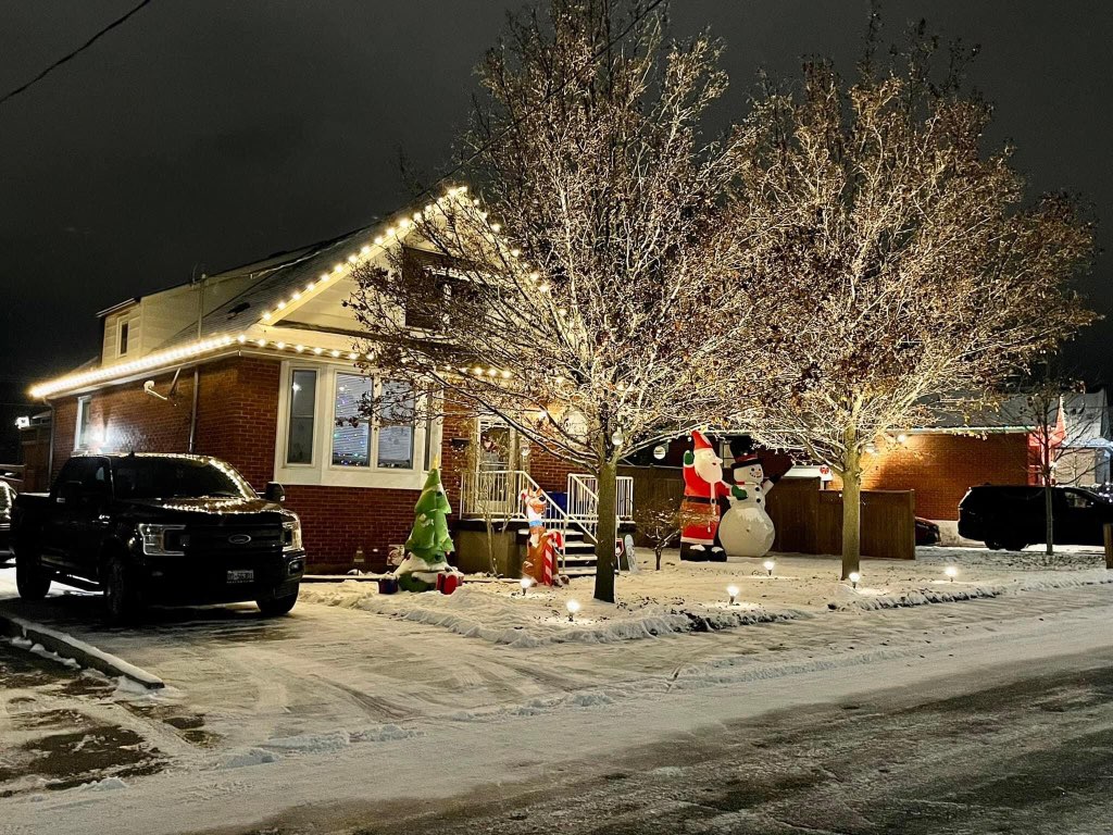 Santa claus in front of a house with lights in the snow.