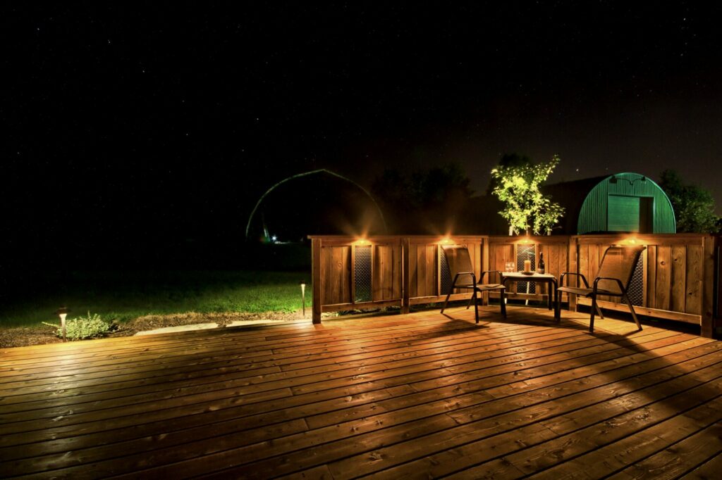 A wooden deck with chairs and a fence at night.