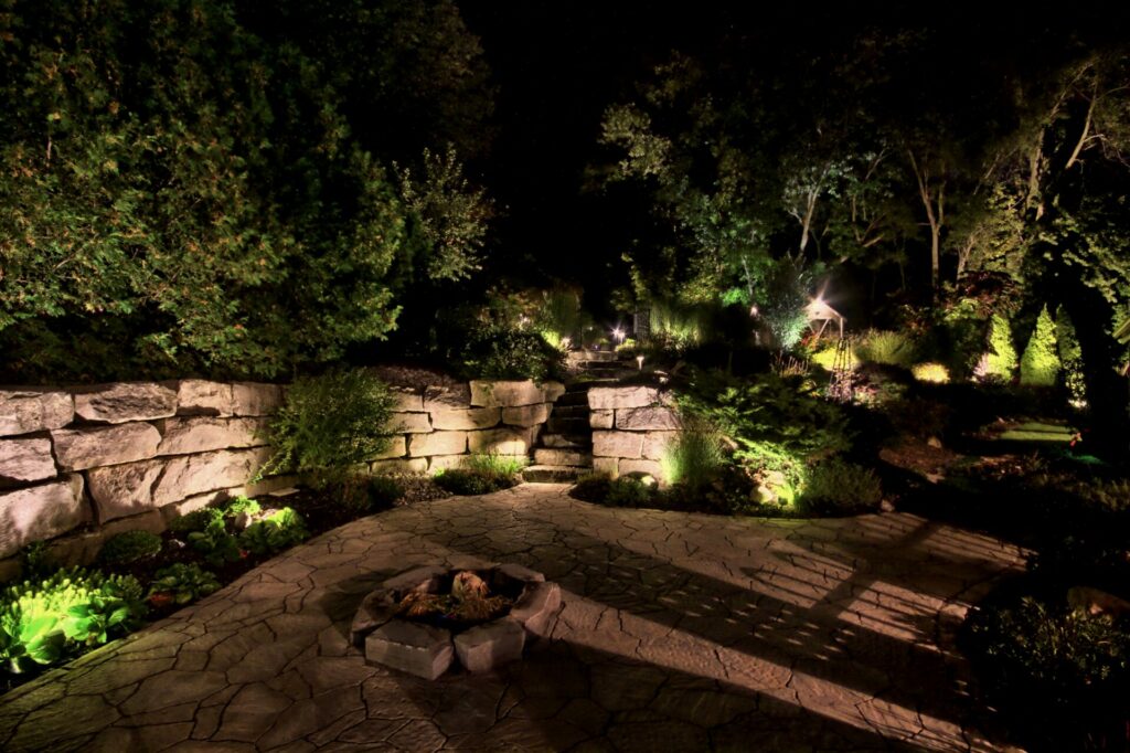 A garden with a fire pit and lighting at night.